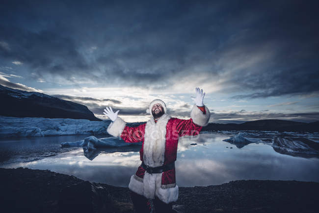 Islanda, uomo mascherato da Babbo Natale in piedi su un ghiacciaio alzando le braccia — Foto stock