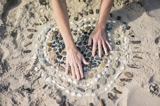 Donna matura che fa un cuore dalle conchiglie sulla spiaggia — Foto stock