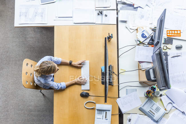 Vue de dessus de la femme utilisant un ordinateur au bureau entouré de documents — Photo de stock