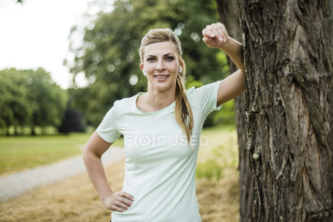 Sorridente sportiva giovane donna appoggiata ad un albero in un parco — Foto stock
