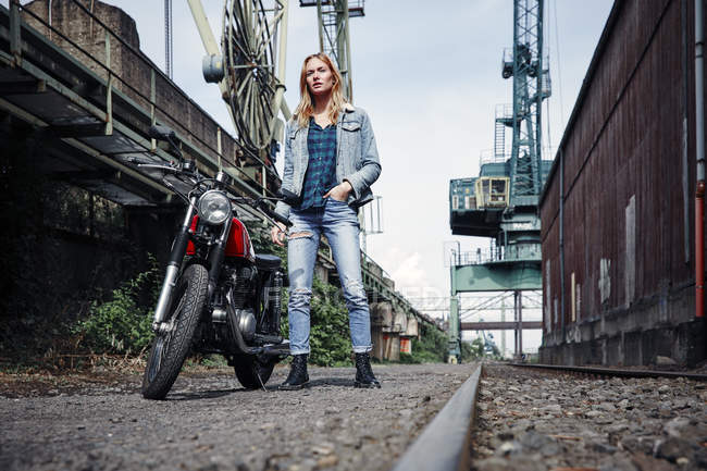 Retrato de jovem mulher confiante em pé ao lado da motocicleta — Fotografia de Stock