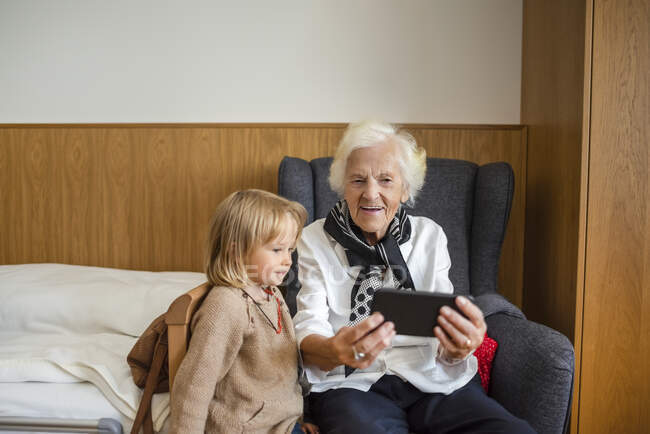 Портрет пожилой женщины, смотрящей вместе с правнучкой фотографии на смартфоне — стоковое фото