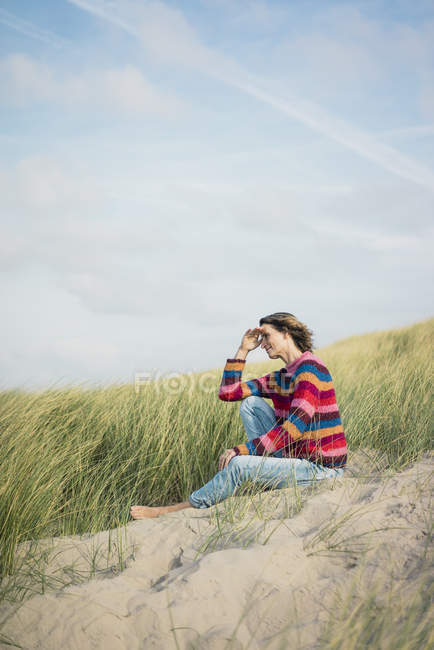 Mujer madura relajándose en la playa, sentada en las dunas - foto de stock