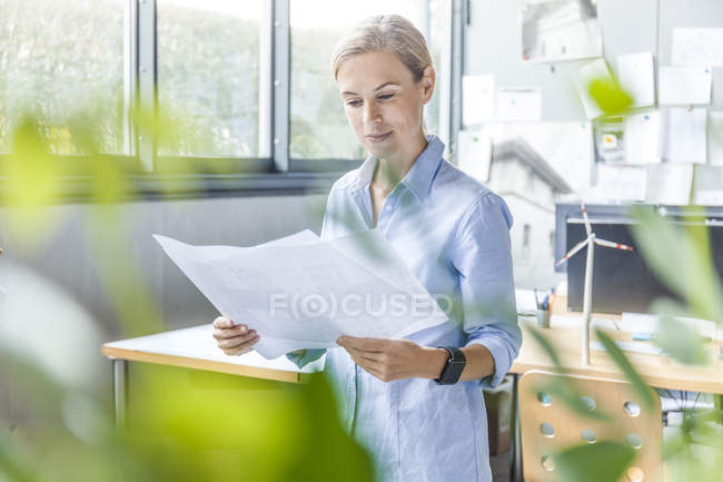 Mulher no escritório trabalhando em plano com modelo de turbina eólica na mesa — Fotografia de Stock