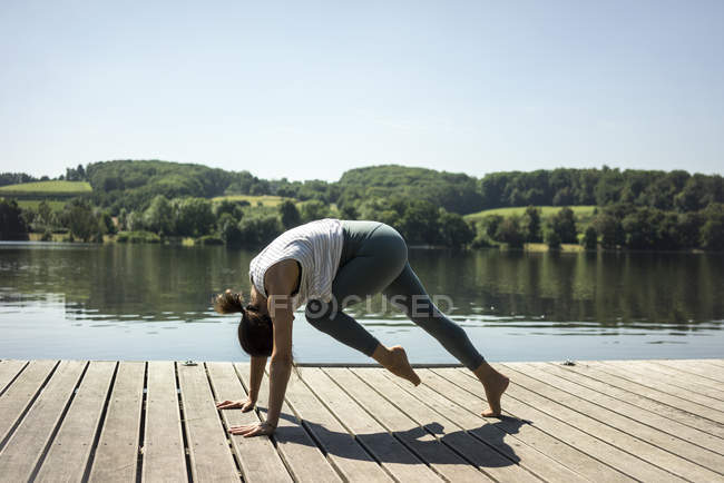 Woman practicing yoga in summer on a jetty at a lake — Stock Photo