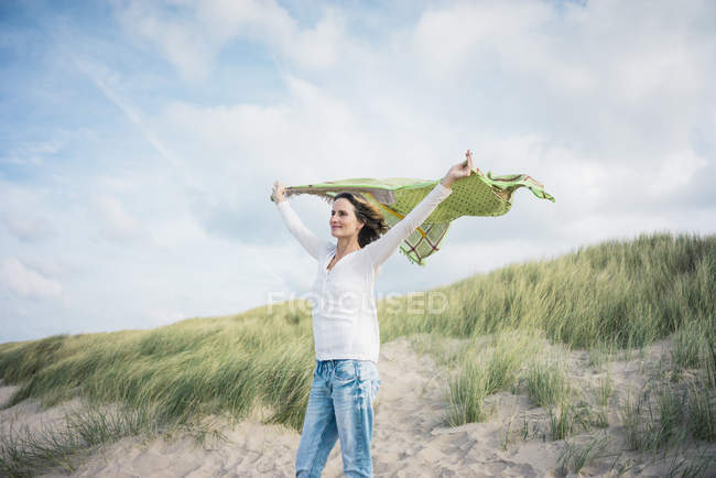 Donna matura che tiene sciarpa battente nel vento, relaxiang tra le dune — Foto stock
