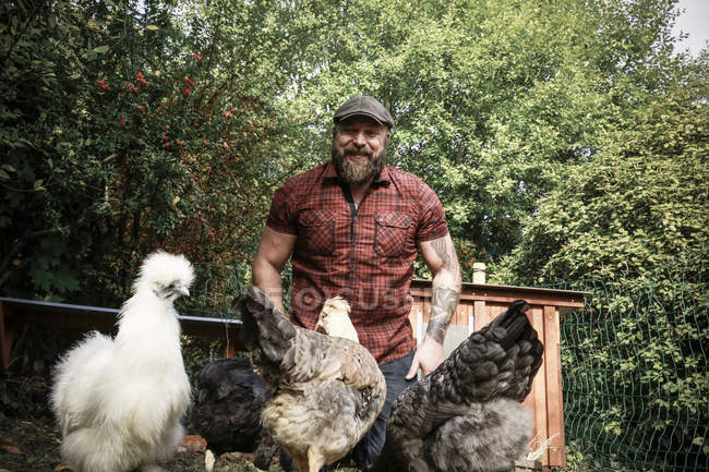 Bärtiger Mann im eigenen Garten mit Hühnern, der in die Kamera schaut — Stockfoto