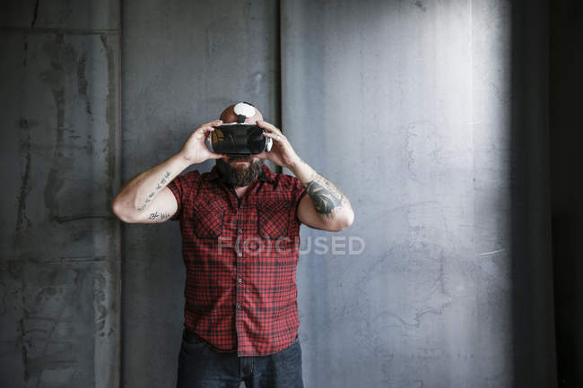 Bearded man wearing and adjusting VR glasses at grey wall — Stock Photo