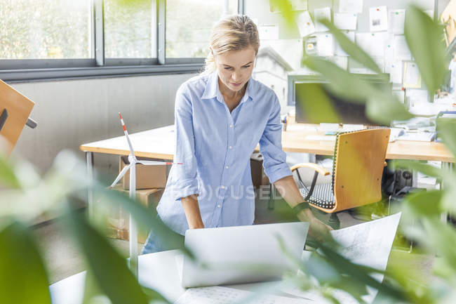 Femme au bureau avec plan, ordinateur portable et éolienne sur la table — Photo de stock