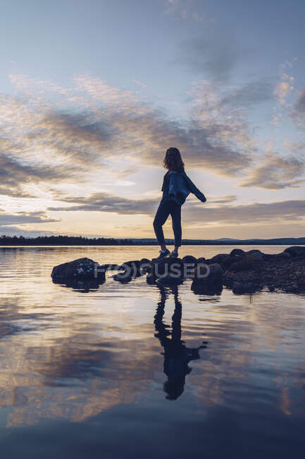 Young woman standing at lake Inari, with arms outstretched, Finland — Stock Photo
