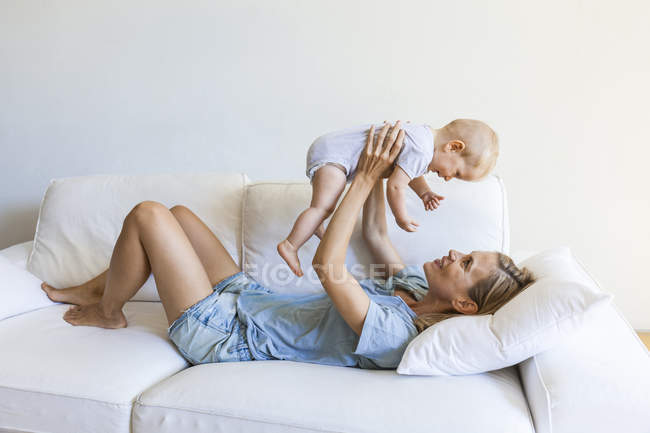 Felice madre sdraiata sul divano e tenendo la sua bambina — Foto stock