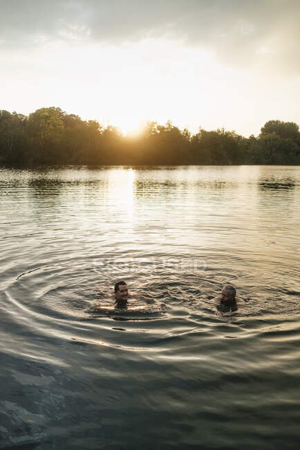 Старий і молодий чоловік плаває в озері на заході сонця — стокове фото