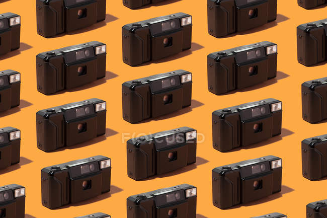 Plastic photo cameras organized in a row over orange background — Stock Photo