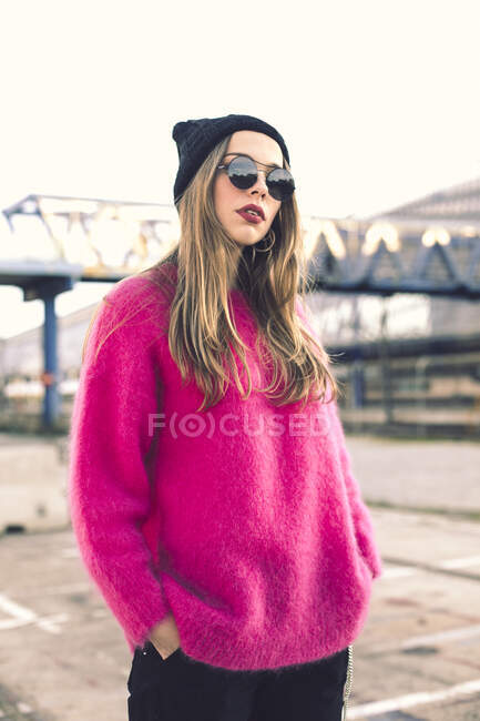 Retrato de mujer joven de moda con gafas de sol, gorra y jersey de punto rosa - foto de stock