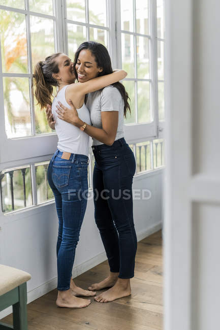 Due amiche felici che si abbracciano alla finestra di casa — Foto stock