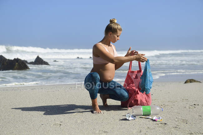 Pregnant woman cleaning the beach from plastic waste — Stock Photo