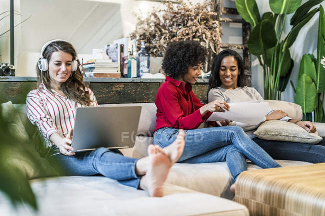 Three women with laptop and documents sitting on couch — Stock Photo
