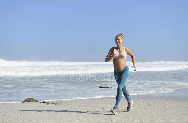 Посмішка вагітної жінки біжить по пляжу. — стокове фото