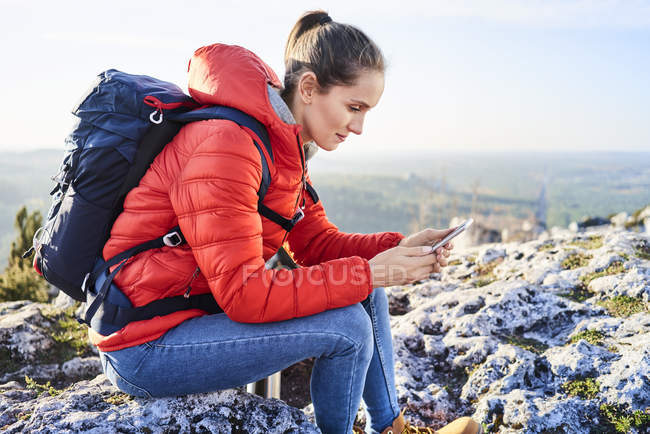 Donna in un viaggio escursionistico in montagna seduto sul telefono cellulare di controllo roccia — Foto stock
