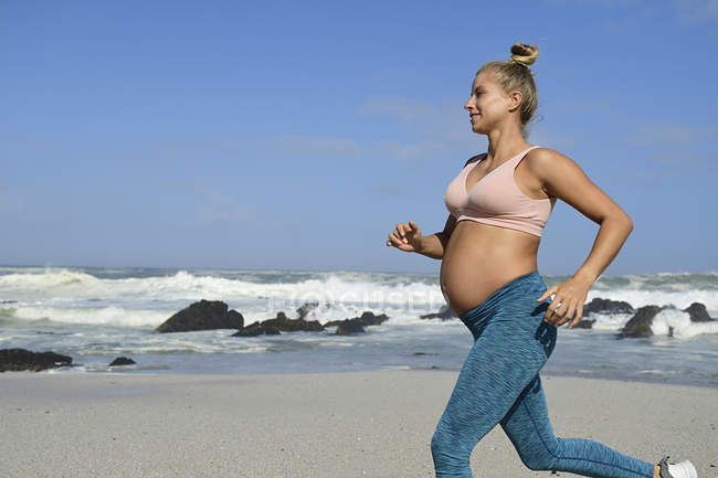 Lächelnde Schwangere beim Joggen am Strand — Stockfoto