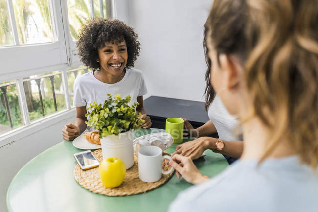 Three happy women sitting at table at home drinking coffee together — Stock Photo