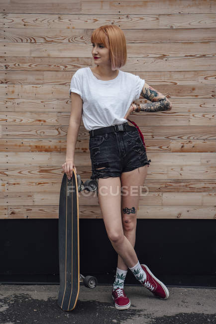 Jeune femme debout au mur en bois avec planche à roulettes sculpteur — Photo de stock
