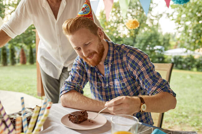 El hombre comiendo pastel en una fiesta de cumpleaños en el jardín — Comida  y bebida, tenedor - Stock Photo | #283050326