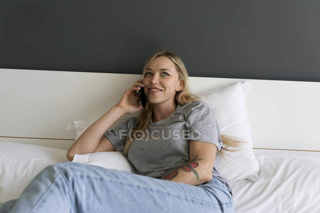 Sorrindo jovem deitada na cama falando no celular — Fotografia de Stock