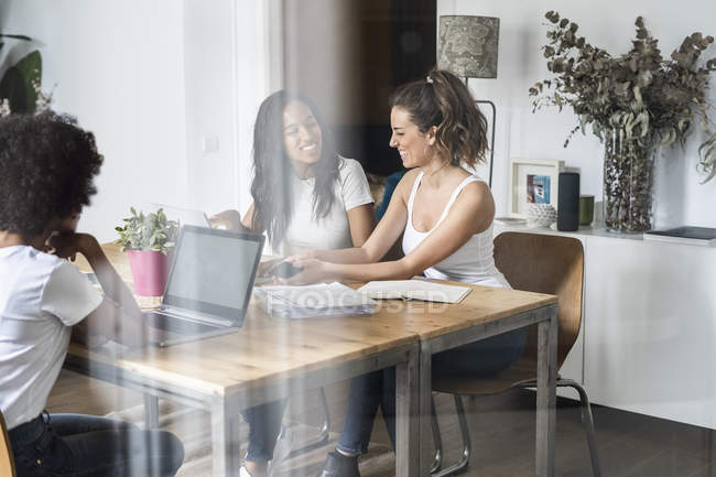 Three women with laptop and documents talking at table — Stock Photo