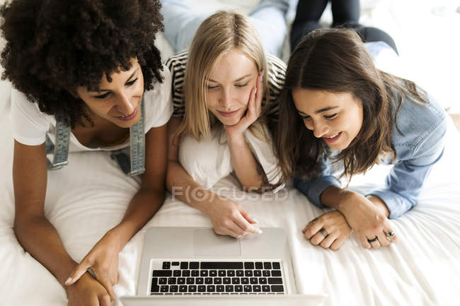 Tre amiche sdraiate sul letto condividendo laptop — Foto stock