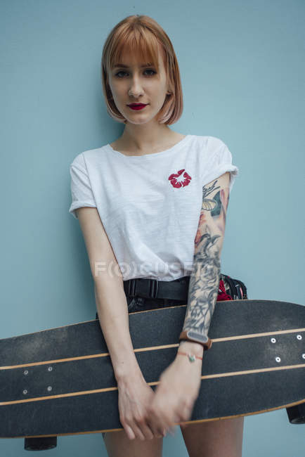 Ritratto di giovane donna fresca che tiene lo skateboard intagliatore in piedi al muro turchese — Foto stock