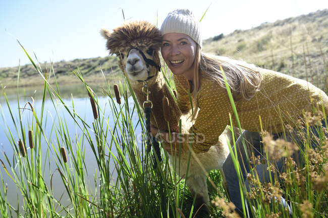 Porträt einer lächelnden blonden Frau Kopf an Kopf mit Alpaka in der Natur — Stockfoto