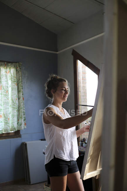 Mujer joven sonriente pintando en su taller - foto de stock