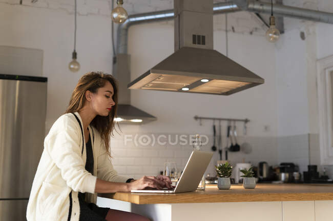 Молода жінка сидить на кухні, використовуючи ноутбук — стокове фото