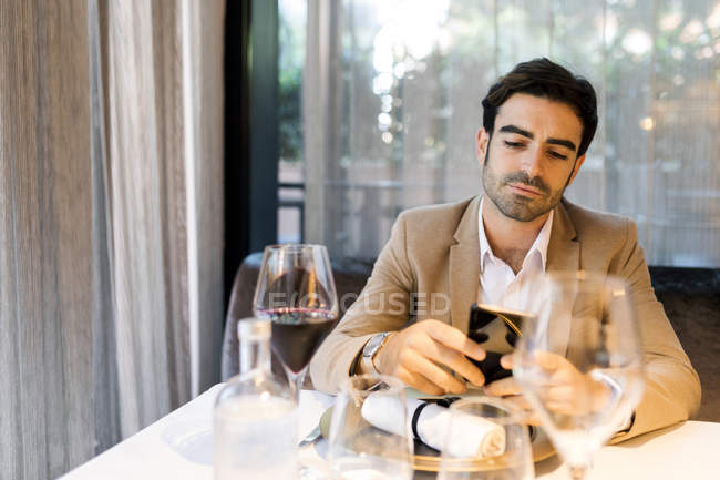 Людина, сидячи за столом у ресторані і за допомогою стільникового телефону — стокове фото
