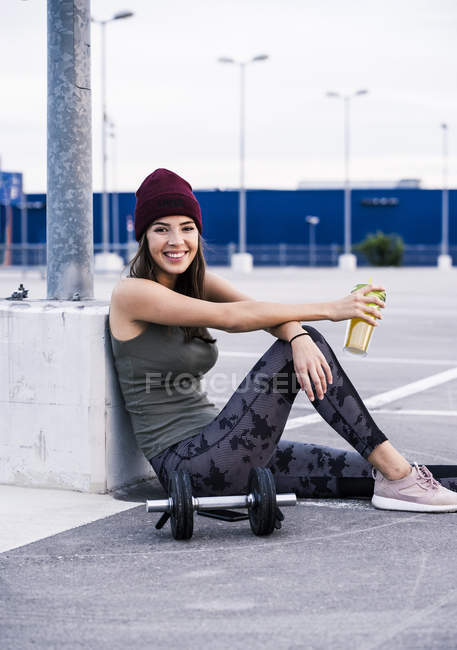 Young woman sitting on ground after dumbbell training, drinking juice — Stock Photo