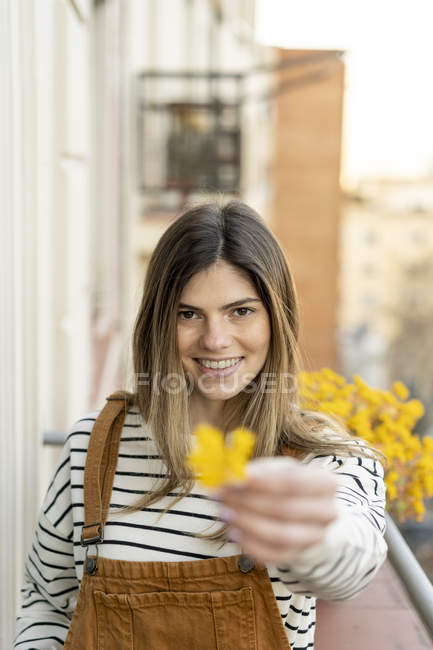Retrato de una joven sonriente en el balcón regalando flor amarilla — Stock Photo