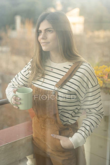 Portrait of smiling young woman with coffee mug standing on balcony — Stock Photo