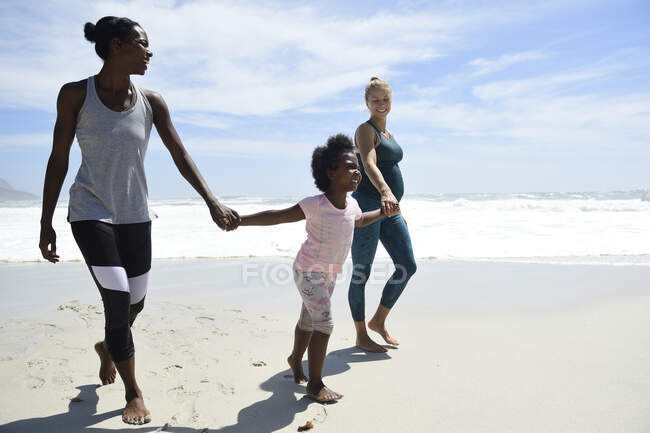 Happy mother with daughter and friend walking on the beach — Stock Photo