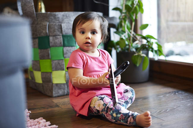 Portrait de bébé fille mignonne assis sur le sol à la maison tenant la télécommande — Photo de stock