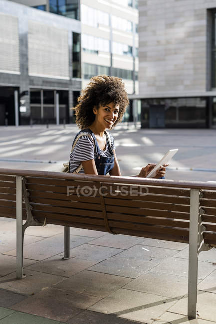 Mittlere erwachsene Frau mit lockigem Haar, auf einer Bank sitzend, mit digitalem Tablet — Stockfoto