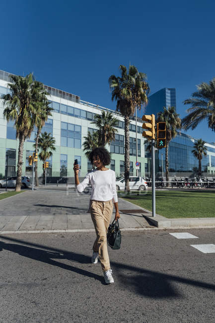 Молодая деловая женщина в городе, используя смартфон, переходя дорогу — стоковое фото