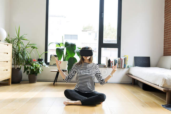 Mujer joven en casa con gafas VR y haciendo yoga - foto de stock