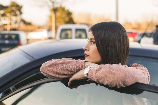 Teenage girl leaning on car door looking at distance — Stock Photo