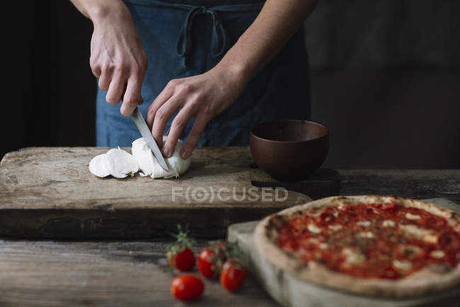 Jovem preparando pizza, cortando mussarela na tábua de cortar — Fotografia de Stock