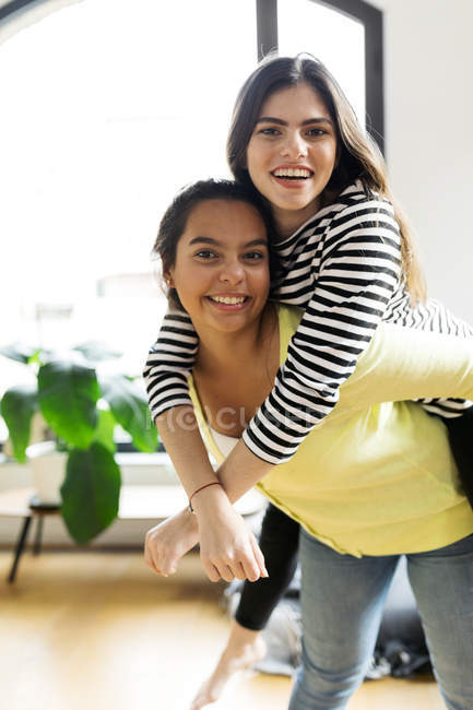 Портрет щасливого молодої жінки проведення подруга piggyback будинку — стокове фото