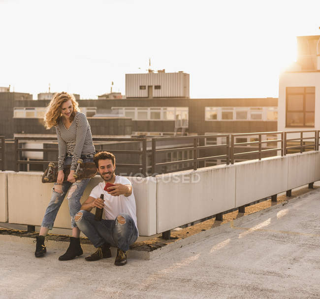 Junges Paar entspannt sich bei Sonnenuntergang auf Dachterrasse und macht Selfie mit Handy — Stockfoto