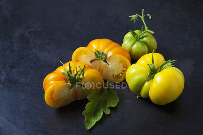 Ganze und in Scheiben geschnittene Asojtschka-Tomaten auf dunklem Boden — Stockfoto