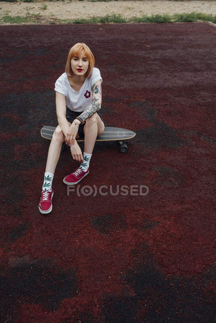 Portrait de jeune femme cool assis sur skateboard sculpteur à l'extérieur — Photo de stock