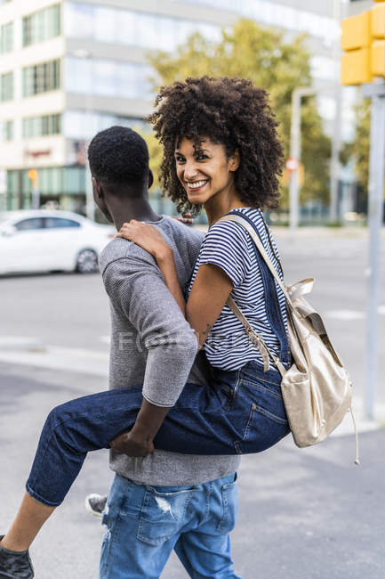 Young man carrying his girlfriend piggyback in the street — Stock Photo